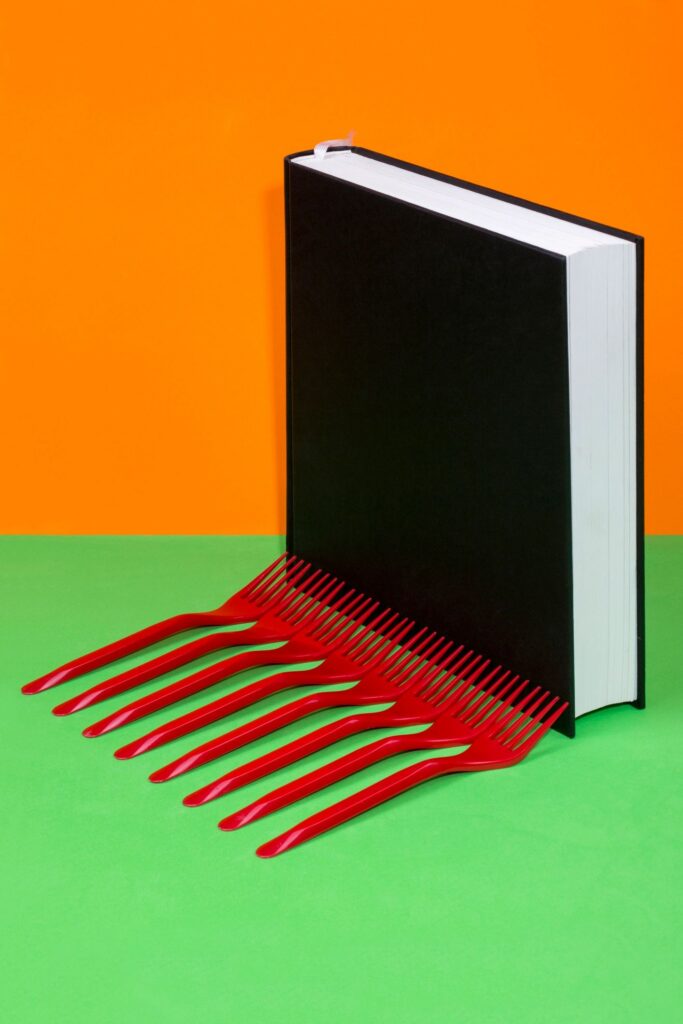 Still life with a black book and red forks on a colored background